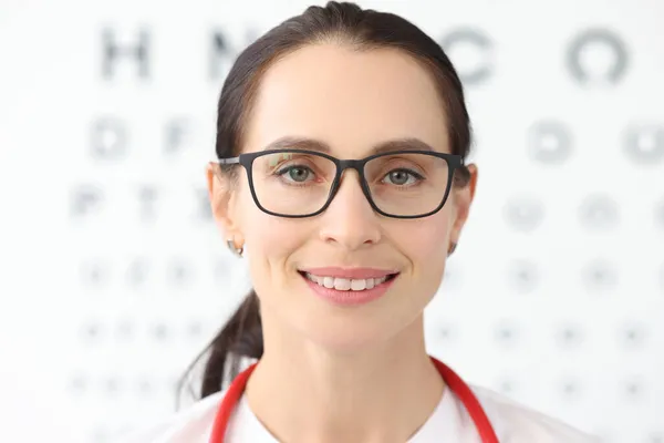 Szemészeti vizsgálat céljára szolgáló táblázat hátterével szemben álló szemüveges női szemész — Stock Fotó