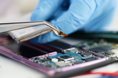 Atölyede kırık telefonun üzerinde mikroçip tutan lastik eldivenler ustası.