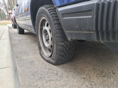 Lastiği patlamış bir araba kaldırıma yakın duruyor.