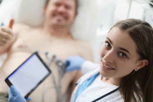 Orvos kardiológus gazdaság digitális tabletta elektrokardiogram a háttérben a betegek ok gesztus — Stock Fotó