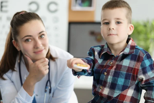 Niño pequeño sosteniendo cápsulas de gelatina amarilla en la cita con el médico — Foto de Stock