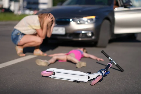 Little girl lies motionless on asphalt with scooter after collision with car — Stock Photo, Image