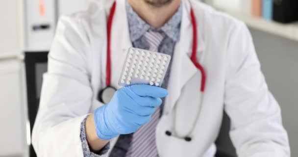 Mann Arzt sitzt am Tisch in der Klinik und zeigt Blister mit Pillen 4k Film Zeitlupe — Stockvideo