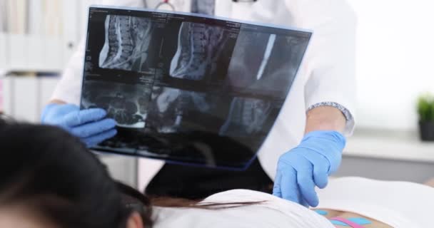 Osteópata palpando los procesos espinales del paciente con cintas kinesio y mirando la radiografía de la columna vertebral 4k película cámara lenta — Vídeos de Stock