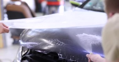 Arabanın kaputunu koruyucu plastik film 4K ağır çekim ile kaplayan usta bir tamirci.