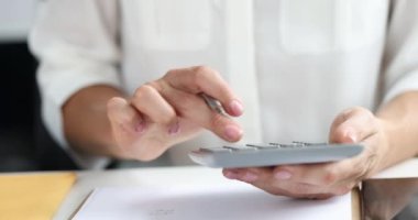 İş kadını, ofis 4k ağır çekimde hesap makinesine güveniyor ve kağıda veri yazıyor.