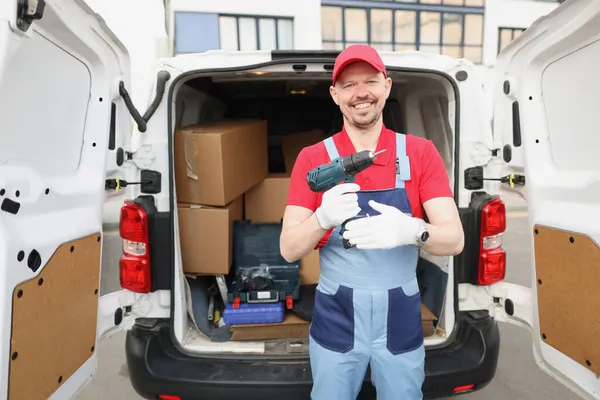 Smiling worker hold screwdriver device in hand in front of truck full of boxes