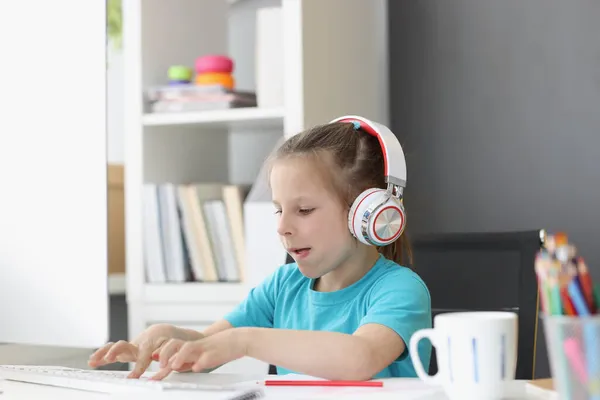 Nettes Kind trägt Kopfhörer und tippt mit Mühe auf der Tastatur — Stockfoto