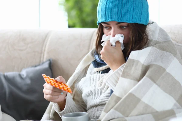 Kvinna med förkylning sitter på soffan med piller och näsduk — Stockfoto