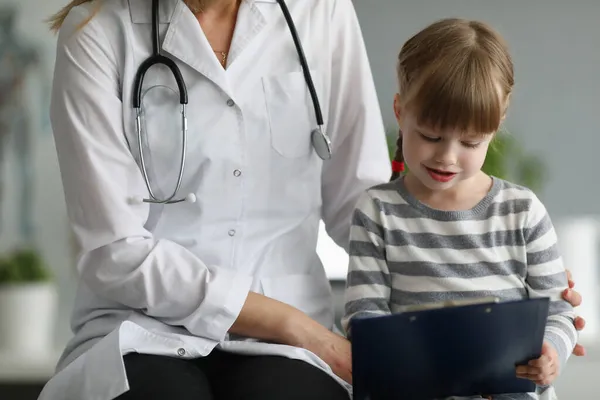 Doktorn sitter bredvid en liten flicka och håller i skrivbordet — Stockfoto