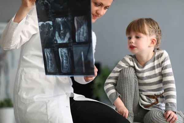 Mujer médico muestra niña una radiografía de columna vertebral —  Fotos de Stock