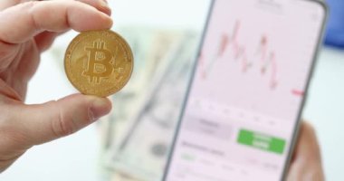 Altın Bitcoin tutan ve cep telefonundaki büyüme grafiklerini izleyen adam 4K yakın plan film