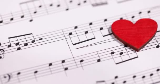 Червоне дерев'яне серце лежить на музичних нотах повільний рух 4k фільм — стокове відео