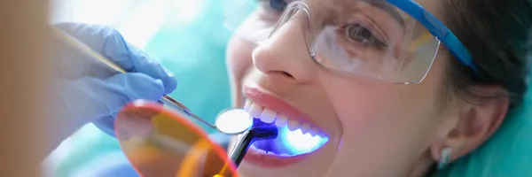 Kobieta w okularach ochronnych leczona u dentysty lampą świetlną — Zdjęcie stockowe