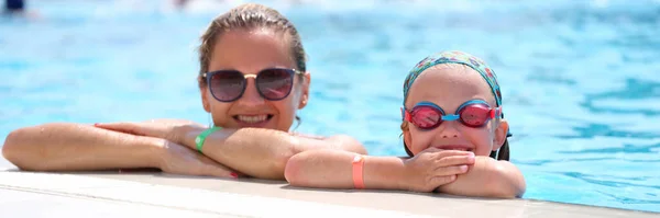 Kleines Mädchen mit Schwimmbrille und Mutter am Beckenrand liegend — Stockfoto