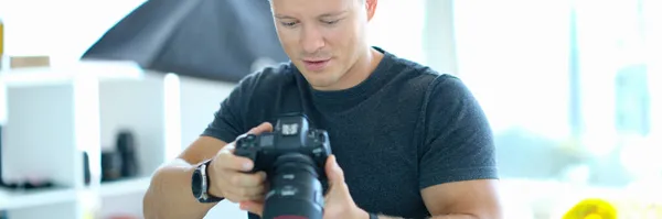 Fotografo maschio che tiene la macchina fotografica professionale nera nelle sue mani in studio — Foto Stock