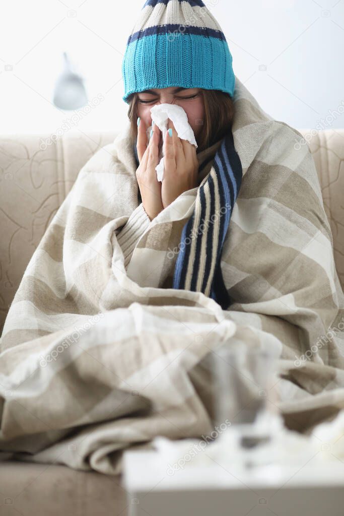 Sick woman blowing running nose and sneezing in tissue at home