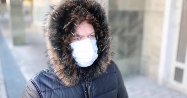 Hombre con abrigo de invierno y capucha con máscara de protección médica camina por la calle. — Vídeo de stock