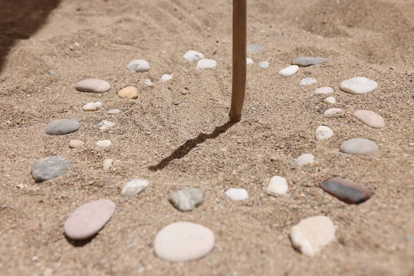 Drewniany kij i kamyki na piasku ukazujące czas przez cień — Zdjęcie stockowe