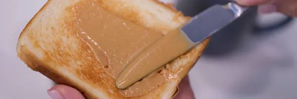 Frau verteilt Erdnussbutter auf Toast in Großaufnahme — Stockfoto