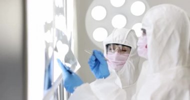 Koruyucu takım elbiseli ve maskeli iki doktor röntgenleri ağır çekimde inceledi.