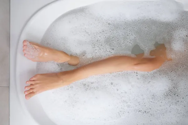 Pernas femininas finas em uma banheira com água ensaboada — Fotografia de Stock