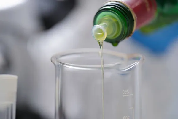 O óleo de uma garrafa é derramado em um recipiente de medição — Fotografia de Stock