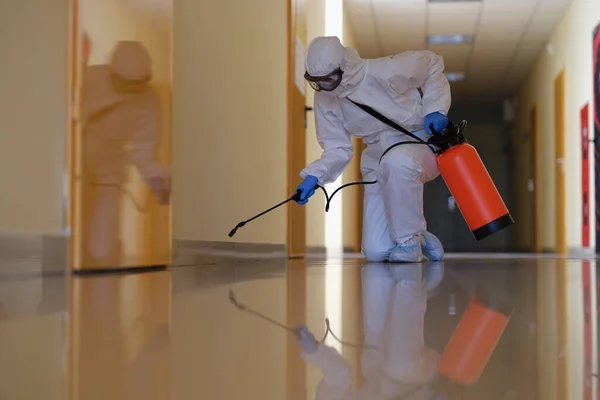 A man in a protective suit splashes on the plinth in the hallway — Stock Photo, Image