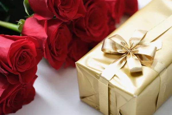 Röda rosenknoppar och en gåva i guldpapper med band — Stockfoto