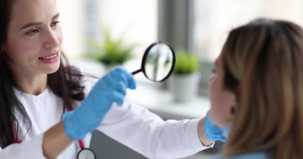 Médico examinando la piel de la cara de la mujer usando lupa película 4k cámara lenta — Vídeo de stock
