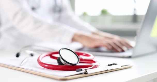 Red stethoscope lying on background of doctor typing on computer keyboard 4k movie slow motion — Stock Video