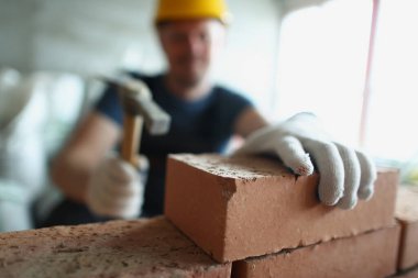 Keskin şapkalı usta, tamamlanmamış yapıya taş koymak için çekiç teçhizatı kullanıyor.