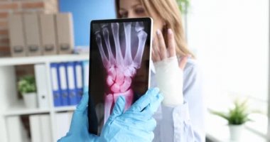 Doktor, bileğinde ağrı olan hastanın elinin röntgeniyle tablet tutuyor.