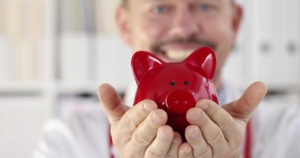 Sorrindo médico está segurando porquinho banco câmera lenta filme 4k — Vídeo de Stock