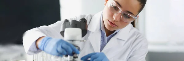 Mujer científica química en gafas protectoras poniendo diapositiva de vidrio en microscopio en laboratorio —  Fotos de Stock