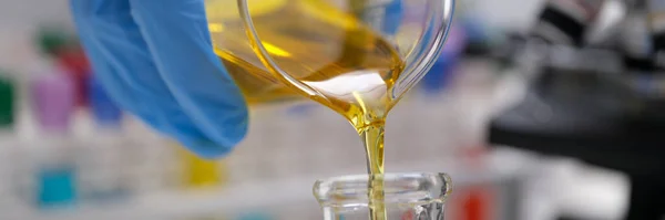 Químico vertiendo aceite comestible del matraz en el primer plano del tubo de ensayo —  Fotos de Stock
