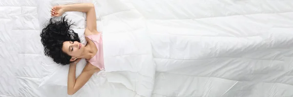 Mujer joven con el pelo rizado durmiendo en la cama blanca vista superior —  Fotos de Stock