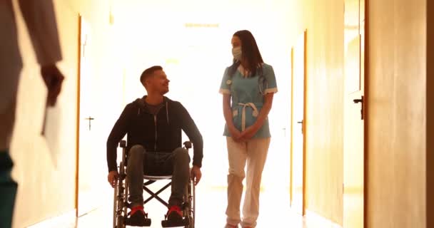 Nővérke sétál a beteg tolószékben a folyosón, és üdvözlő orvos 4K film lassított felvétel — Stock videók