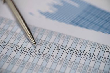 Dökümanların üzerine uzanan metal kalem ve yakın plan grafikler