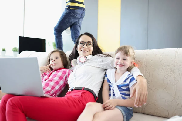 Szczęśliwa kobieta pozowanie z dziećmi na kanapie podczas pracy na laptopie — Zdjęcie stockowe
