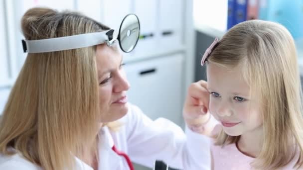 Ent met frontale reflector onderzoeken van kleine meisje oor met behulp van otoscoop 4k film slow motion — Stockvideo
