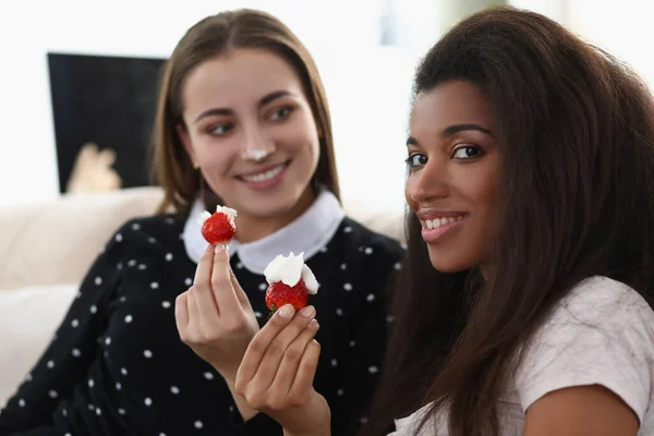 Uśmiechnięte dziewczyny jedzące smaczne świeże truskawki pokryte bitą śmietaną — Zdjęcie stockowe