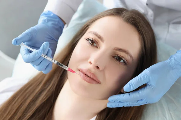 Jonge vrouw krijgt injectie van botox in haar lippen, cosmetoloog met behulp van spuit — Stockfoto