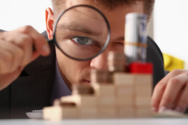 Homme d'affaires tient dans la main loupe noire regarde tour de pièces placées sur des cubes en bois — Photo