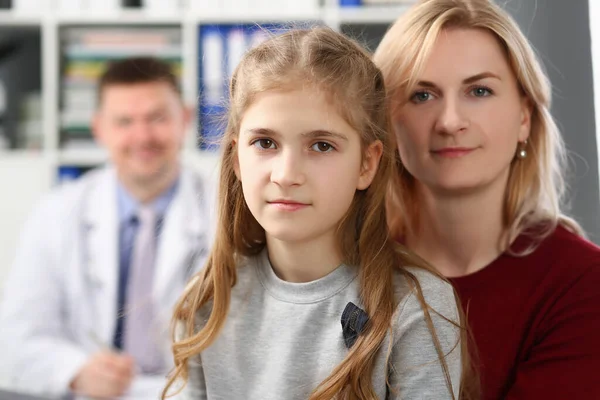 Мать и дочь на приеме у врача, медицинский работник улыбается сзади — стоковое фото