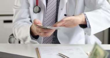 Beyaz önlüklü doktor onları dağıtırken dolarları sayıyor.