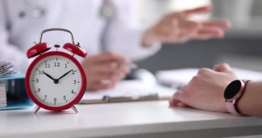 Doktor, alarmlı saatin arka planına karşı hastaya tıbbi danışmanlık yapar.