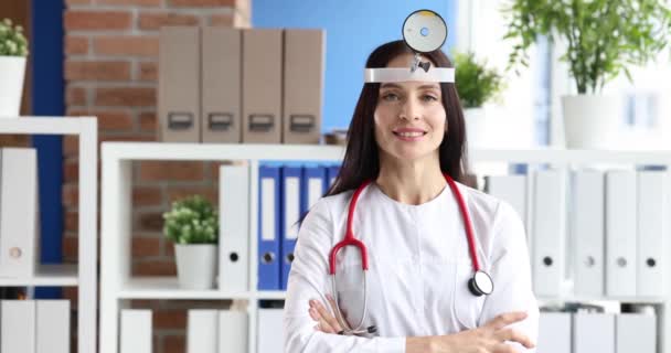 Mujer sonriente otorrinolaringólogo con reflector en la frente en el consultorio — Vídeos de Stock
