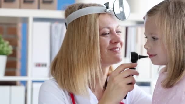Врач-энтоскоп с фронтальным отражателем смотрит на ухо маленькой девочки с помощью фотоскопа 4К фильм замедленной съемки — стоковое видео