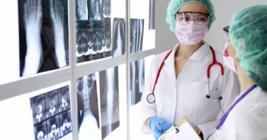 Koruyucu maskeli ve gözlüklü kadınlar klinikteki röntgenlere bakıyor. Ağır çekim.